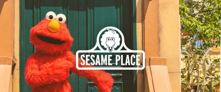 The Sesame Place logo over a picture of Elmo standing on the stairs outside