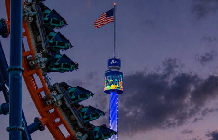 Roller coaster at night in front of a tower with an American Flag