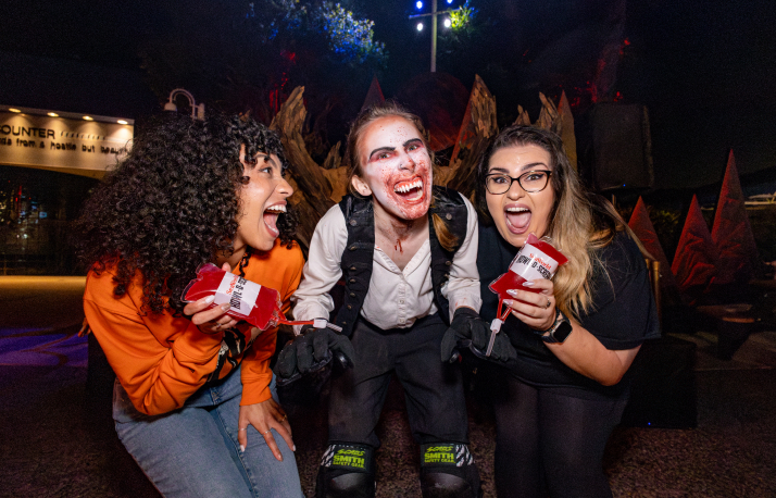Two scared people holding blood bags next to a halloween scare actor