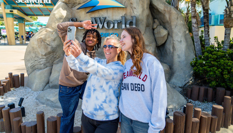 Group of three people taking a selfie in front of a SeaWorld sign