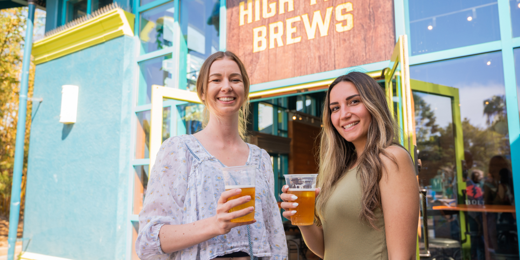 Two women holding beers in front of High Tide Brews