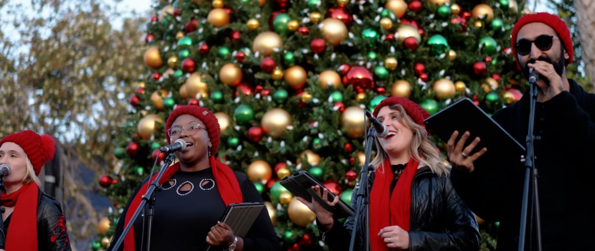A group of Christmas carolers in front of a Christmas tree