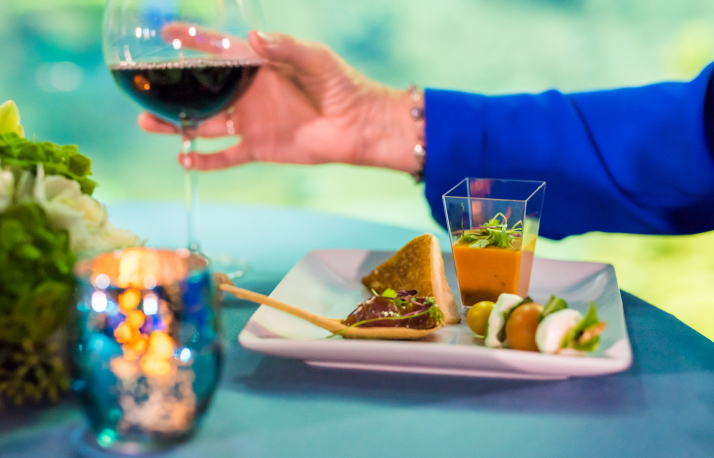 A place setting with some food and a hand holding a wine glass