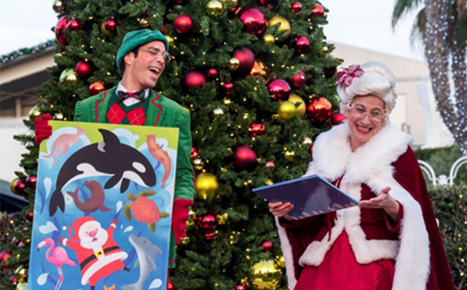 Mrs. Claus and an elf telling a story in front of a Christmas tree at SeaWorld San Diego